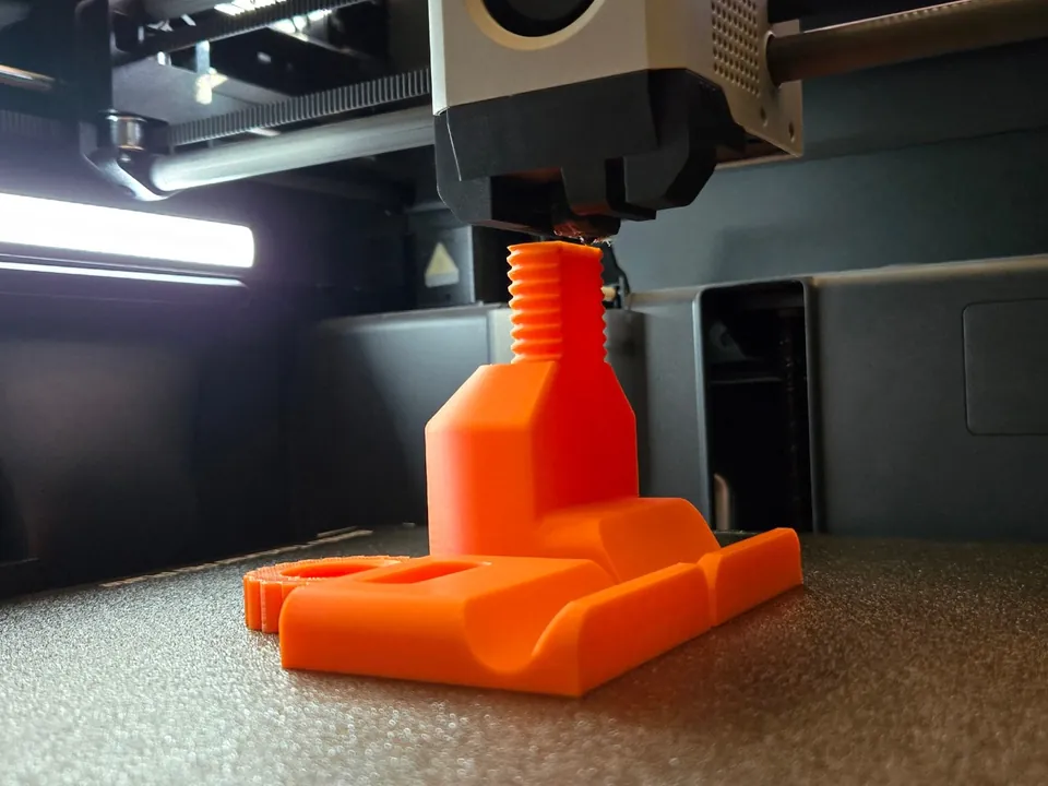 An orange part with a printed screw thread being finished inside the printer